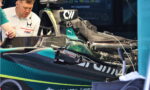 Mechanic with headset inspects a teal-black Formula 1 car in the pit area during a race setup.