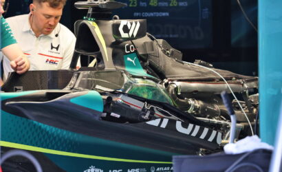 Mechanic with headset inspects a teal-black Formula 1 car in the pit area during a race setup.