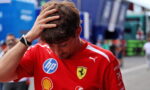 Man in a red Ferrari shirt runs his hand through his hair in a pit lane garage with sponsor logos visible.