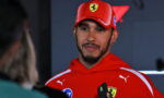 Man in a red Ferrari cap and hoodie being interviewed, holding a phone, with interviewer in foreground left.