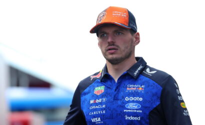 Portrait of a Formula 1 driver wearing an Oracle Red Bull Racing polo and an orange cap, looking off to the side.