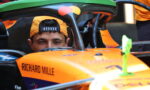 Driver wearing an orange cap sits in an orange race car cockpit labeled Richard Mille.