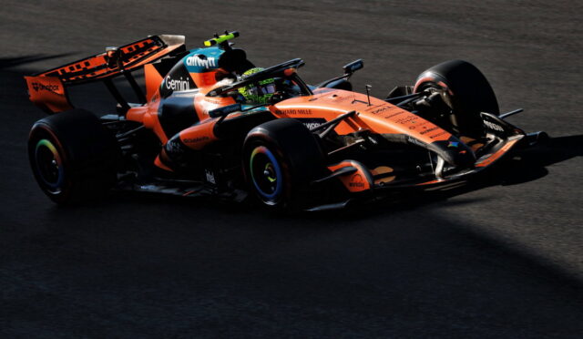 Orange Formula 1 car on a dark track, branding and sponsor logos visible as it corners.