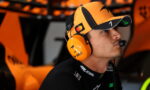 Race car driver in an orange cap and matching headset, focused in the pit area.