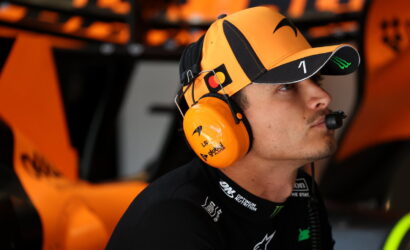 Race car driver in an orange cap and matching headset, focused in the pit area.