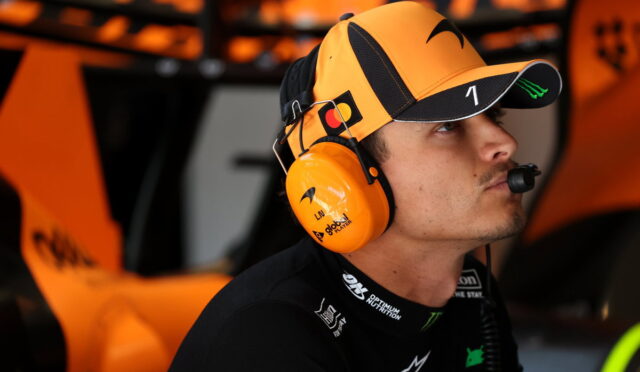 Race car driver in an orange cap and matching headset, focused in the pit area.