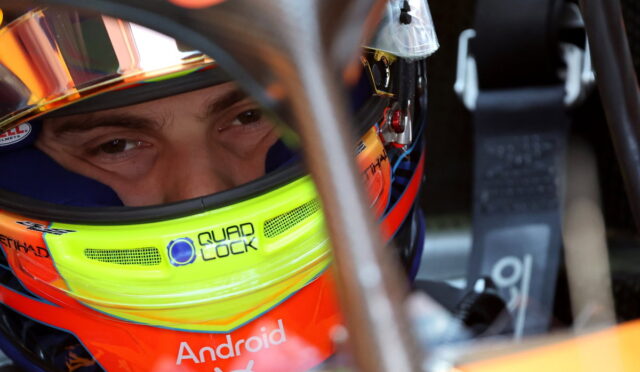 Close-up of a race car driver wearing a bright neon-yellow helmet with Android text, seen through the helmet visor inside a cockpit.