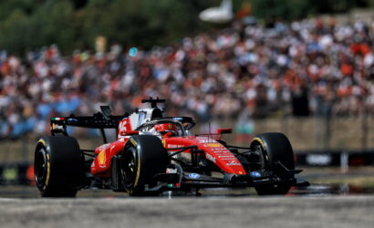 Red Ferrari Formula 1 car racing on a track with a blurred crowd in the stands behind it.