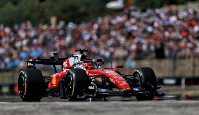 Red Ferrari Formula 1 car racing on a track with a blurred crowd in the stands behind it.