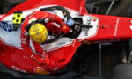 Top-down view of a red Ferrari Formula 1 car with a yellow-helmeted driver in the cockpit, showing sponsor logos like HP and Bitdefender.