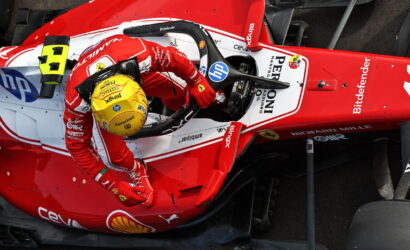 Top-down view of a red Ferrari Formula 1 car with a yellow-helmeted driver in the cockpit, showing sponsor logos like HP and Bitdefender.