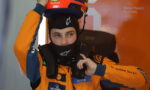 Race car driver in an orange-blue suit adjusting a helmet on their head, sponsor logos visible (DP World, Cisco).