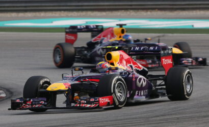 Two Red Bull Racing Formula 1 cars race side by side on a track, with branding from Infiniti and Total visible on the cars.