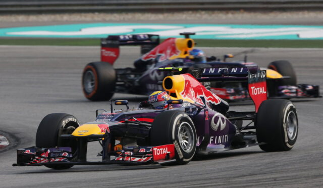 Two Red Bull Racing Formula 1 cars race side by side on a track, with branding from Infiniti and Total visible on the cars.