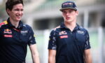Two men in Red Bull Racing polo shirts walk and chat at a race track, smiling.