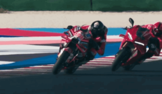 Two red racing motorcycles lean into a corner on a racetrack, riders in red gear close together.