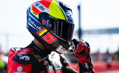 Close-up of a motorcycle racer in a colorful helmet adjusting his visor.