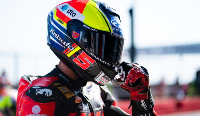 Close-up of a motorcycle racer in a colorful helmet adjusting his visor.