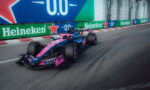 Formula 1 car in pink and blue livery speeding along a street circuit with Heineken banners in the background