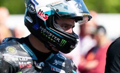 Motorcycle racer in a full-face helmet with Monster Energy and sponsor logos, ready at the track.