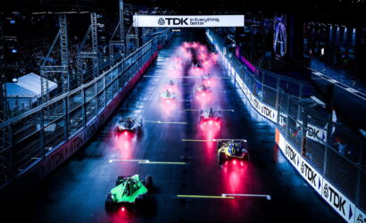 Racing cars at a night-start on a wet track, red exhaust glow trailing behind them under a TDK banner.