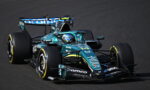 A teal Aston Martin Formula 1 car #14 speeding on a race track with sponsor logos visible on the bodywork.