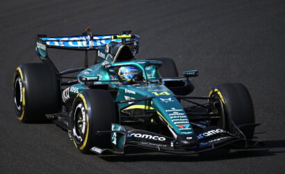 A teal Aston Martin Formula 1 car #14 speeding on a race track with sponsor logos visible on the bodywork.