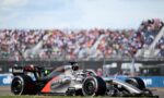 A silver Formula 1 car with Revolut branding speeding on the track, crowd-filled grandstands blurred in the background.