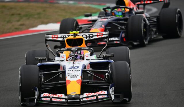 Front-row Formula 1 car with orange nose and Red Bull livery leading a pack on a race track; sponsor logos visible on the car’s nose and wings.