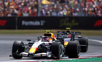 Two Formula 1 cars race on a track with a large cheering crowd in the stands.