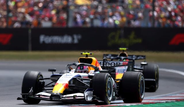 Two Formula 1 cars race on a track with a large cheering crowd in the stands.