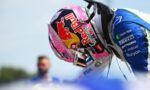 Close-up of a colorful racing helmet with Red Bull branding, attached to a blue racing suit, against a bright sky.