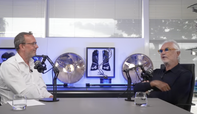 Two men in a podcast studio sit across from each other with microphones, glasses of water, and sports memorabilia in the background.