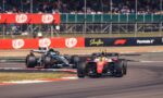 Two Formula 1 cars race on a track with grandstands filled with spectators in the background.