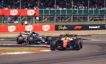 Two Formula 1 cars race on a track with grandstands filled with spectators in the background.