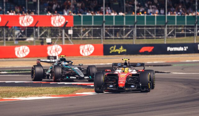 Two Formula 1 cars race on a track with grandstands filled with spectators in the background.