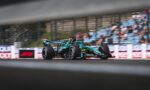 Formula 1 car racing at speed on a track, with a blurred grandstand crowd in the background and motion blur on the wheels.