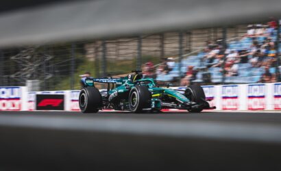 Formula 1 car racing at speed on a track, with a blurred grandstand crowd in the background and motion blur on the wheels.