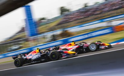 Two Red Bull Racing Formula 1 cars race side by side on a track with a blurred grandstand backdrop due to motion blur.