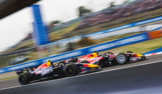 Two Red Bull Racing Formula 1 cars race side by side on a track with a blurred grandstand backdrop due to motion blur.