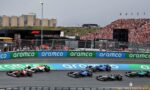 Formula 1 race in progress: several F1 cars cornering on a track with a packed grandstand and sponsor barriers along the wall.