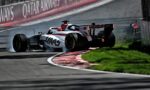 White and black Formula 1 car slides across the track, smoke from the rear tires near red-and-white curbs beside a Qatar Airways barrier.