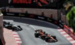 Formula 1 cars race along Monaco’s street circuit, tight barrier walls with sponsor banners (Formula 1, Monaco, Lenovo), spectators in red uniforms watch from the sides