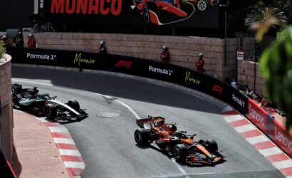 Formula 1 cars race along Monaco’s street circuit, tight barrier walls with sponsor banners (Formula 1, Monaco, Lenovo), spectators in red uniforms watch from the sides