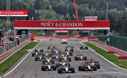 Starting grid of Formula 1 cars on a track, with Moët & Chandon branding overhead and green forest backdrop.
