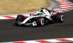 White Formula 1 race car speeds around a corner on a track with red-and-white curbs visible in the foreground and background.