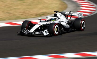 White Formula 1 race car speeds around a corner on a track with red-and-white curbs visible in the foreground and background.