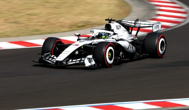 White Formula 1 race car speeds around a corner on a track with red-and-white curbs visible in the foreground and background.
