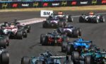 Formula 1 race cars clustered on a track, speeding past sponsor barriers in a tight pack.