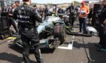 Mercedes race car in pit lane with crew members and engineers working on it, banners and grandstands in the background